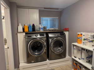 Laundry room featuring washing machine and dryer, cabinet space, and light tile patterned floors