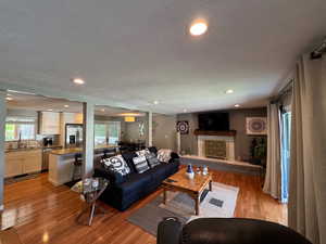 Living room with light wood-style floors, a textured ceiling, recessed lighting, and a fireplace with raised hearth