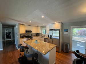 Kitchen featuring appliances with stainless steel finishes, a kitchen island, dark wood finished floors, a textured ceiling, and white cabinetry