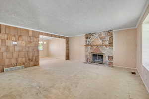 Unfurnished living room featuring a textured ceiling, a chandelier, wood walls, ornamental molding, and a stone fireplace