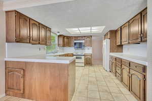 Kitchen with white appliances, wallpapered walls, a peninsula, light tile patterned floors, and a textured ceiling