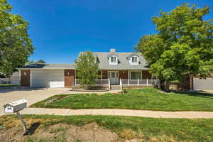 Cape cod home with brick siding, concrete driveway, a garage, a porch, and a front lawn