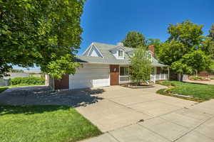 View of front of home with brick siding, covered porch, driveway, a front lawn, and an attached garage