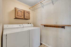 Laundry room featuring washing machine and dryer, cabinet space, wallpapered walls, and light tile patterned floors