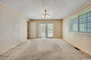 Unfurnished room featuring a chandelier, a textured ceiling, carpet flooring, french doors, and crown molding
