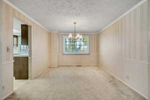 Unfurnished dining area featuring wallpapered walls, crown molding, a chandelier, carpet, and a textured ceiling