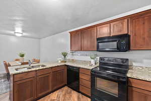 Kitchen with black appliances, a peninsula, light wood-style flooring, light stone counters, and a textured ceiling