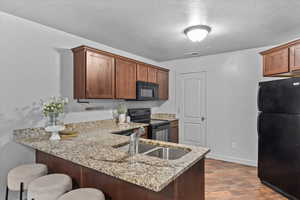 Kitchen featuring black appliances, a peninsula, a kitchen breakfast bar, light stone countertops, and dark wood finished floors