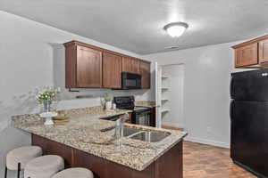 Kitchen featuring black appliances, a peninsula, a kitchen breakfast bar, light stone countertops, and dark wood-type flooring
