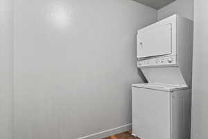 Laundry area featuring stacked washer and clothes dryer and dark wood-type flooring