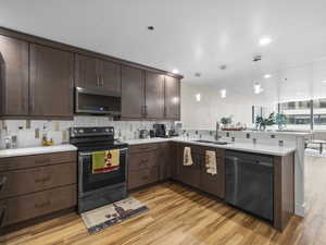 Kitchen with stainless steel microwave, black electric range, dishwasher, pendant lights over breakfast bar, and light wood-style floors