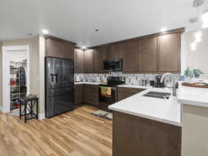 Kitchen featuring appliances with stainless steel finishes, light wood-type flooring, backsplash, light countertops, and dark brown cabinetry