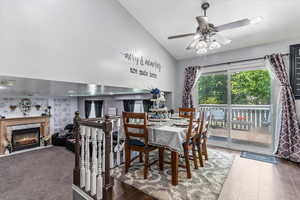 Dining area with ceiling fan, high vaulted ceiling, a premium fireplace, and wood finished floors