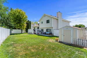 Back of house featuring a shed, a fenced backyard, a chimney, and a deck