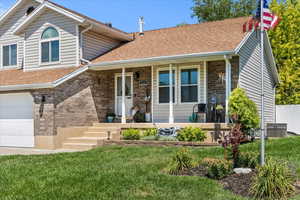 View of front of property with a shingled roof, a garage, brick siding, covered porch, and a front lawn