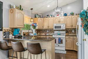 Kitchen featuring white appliances, a peninsula, light brown cabinets, a kitchen bar, and backsplash