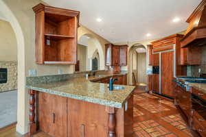 Kitchen featuring paneled built in refrigerator, custom range hood, stainless steel gas stovetop, arched walkways, and recessed lighting