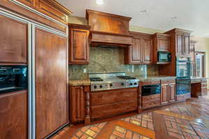 Kitchen featuring black appliances, a warming drawer, tasteful backsplash, custom range hood, and recessed lighting