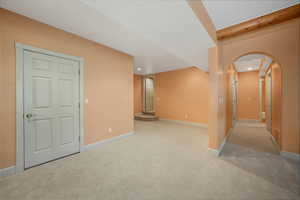Carpeted empty room featuring arched walkways, recessed lighting, and beamed ceiling