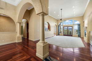 Foyer entrance with ceiling fan, wood finished floors, arched walkways, ornate columns, and a towering ceiling