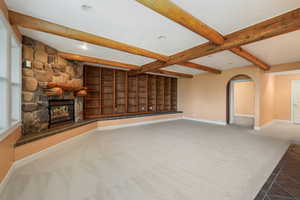 Living room featuring beamed ceiling, carpet floors, a stone fireplace, arched walkways, and recessed lighting