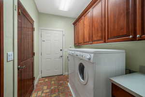 Laundry area with cabinet space, washing machine and dryer, and brick floors