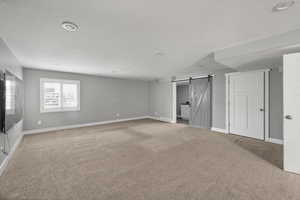 Basement with a barn door, carpet floors, recessed lighting, and a textured ceiling
