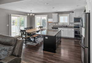Kitchen with appliances with stainless steel finishes, a chandelier, white cabinetry, dark wood-style flooring, and healthy amount of natural light