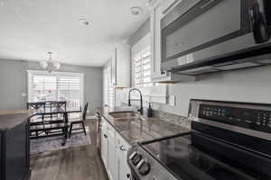 Kitchen with stainless steel appliances, dark wood finished floors, white cabinetry, dark stone counters, and decorative light fixtures