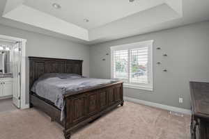 Bedroom with a raised ceiling, light colored carpet, and connected bathroom