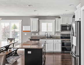 Kitchen with appliances with stainless steel finishes, dark wood finished floors, dark stone counters, white cabinets, and a center island