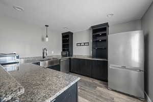 Kitchen featuring stainless steel appliances, light wood-style floors, light stone counters, recessed lighting, and dark cabinets