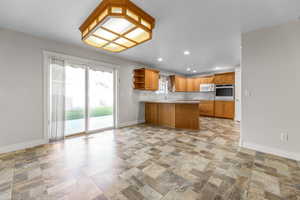 Kitchen with open shelves, a peninsula, recessed lighting, stone finish floors, and light countertops