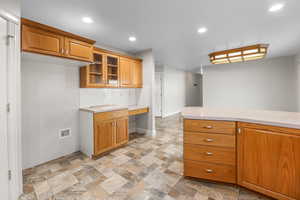 Kitchen featuring glass insert cabinets, brown cabinetry, stone finish floors, recessed lighting, and decorative backsplash