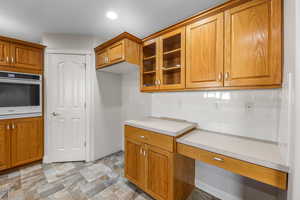 Kitchen with wall oven, brown cabinets, glass insert cabinets, backsplash, and recessed lighting