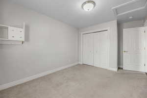 Unfurnished bedroom with carpet, attic access, a closet, and a textured ceiling