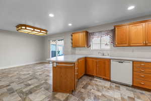 Kitchen featuring brown cabinetry, dishwasher, light countertops, a peninsula, and recessed lighting