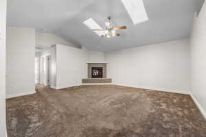 Unfurnished living room with lofted ceiling, dark carpet, a fireplace, ceiling fan, and a skylight