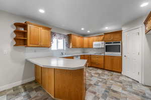 Kitchen featuring brown cabinetry, white appliances, stone finish flooring, light countertops, and a peninsula