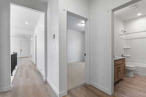 Hall with light wood finished floors and recessed lighting