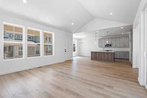 Kitchen featuring open floor plan, stainless steel microwave, gray cabinetry, a kitchen island with sink, and light countertops