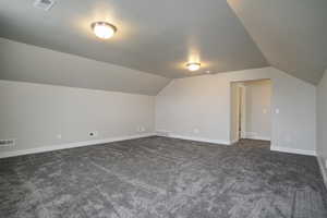 Additional living space featuring lofted ceiling and dark carpet