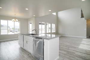 Kitchen with dishwasher, a center island with sink, a chandelier, light wood-type flooring, and white cabinets