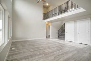 Unfurnished living room featuring a towering ceiling, stairs, ceiling fan, and wood finished floors