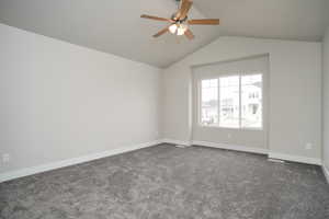 Spare room with ceiling fan, dark carpet, and lofted ceiling