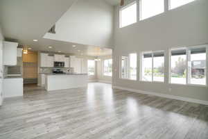 Unfurnished living room featuring healthy amount of natural light, a chandelier, light wood-style flooring, a high ceiling, and recessed lighting