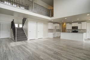 Unfurnished living room featuring a towering ceiling, light wood-style flooring, stairway, and recessed lighting