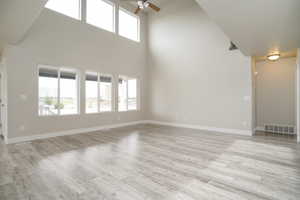 Unfurnished living room featuring ceiling fan, a towering ceiling, and light wood finished floors