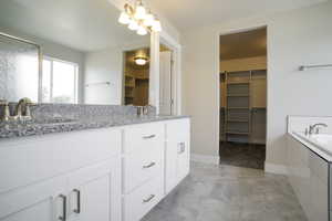 Bathroom with double vanity, a spacious closet, a garden tub, and a shower with door