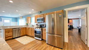 Kitchen with stainless steel appliances, light wood-type flooring, natural finished wood cabinetry, tasteful backsplash, and a peninsula